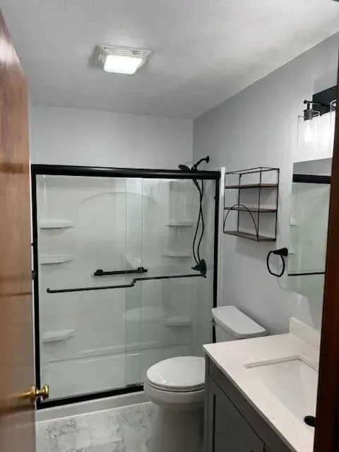 Bathroom with a gray vanity, toilet, and black-framed shower. Light gray walls and door.