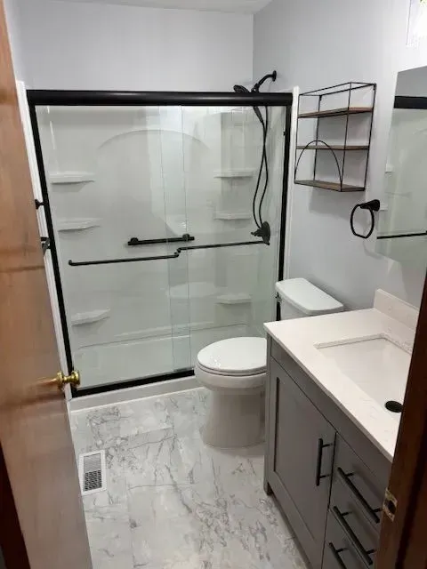 Bathroom with gray vanity, white toilet, glass shower, black fixtures, and light gray tiled floor.