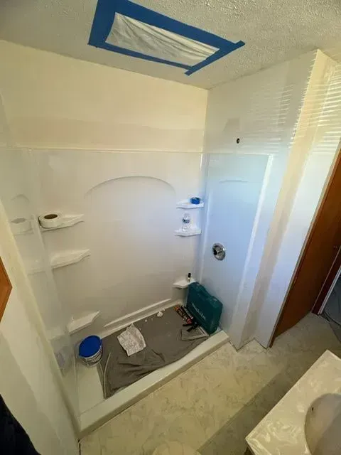 White shower stall with shelves and a skylight in a bathroom; a blue toolbox sits inside.