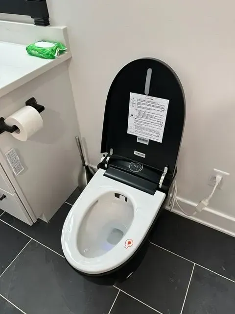 A modern white and black bidet toilet in a bathroom, with a partially open lid.