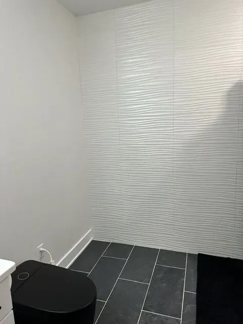 Small modern bathroom with a black toilet, dark tile floor, and white textured wall.
