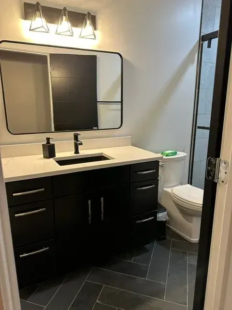 Modern bathroom with black vanity, white countertop, rectangular mirror, and gray tiled floor.
