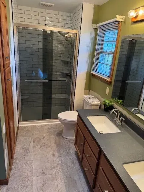 Bathroom with a shower, toilet, sink, and dark wood vanity. Gray tile floor and white brick shower tile.