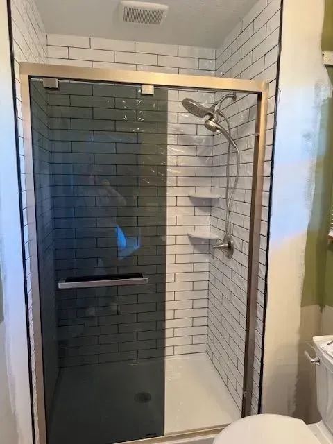 Shower with white brick-like tiles, a glass door, and a silver shower head and shelves.