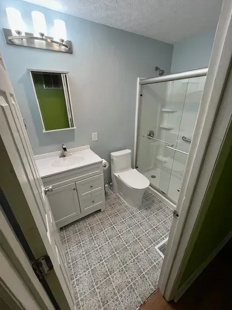 Bathroom with white vanity, toilet, and shower, blue walls, patterned floor tiles, and a mirrored medicine cabinet.
