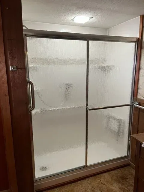 A frosted glass shower with sliding doors in a bathroom with brown trim.