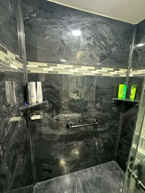 A dark, marbled shower with soap shelves and a horizontal towel bar; bottles of shampoo and body wash are visible.