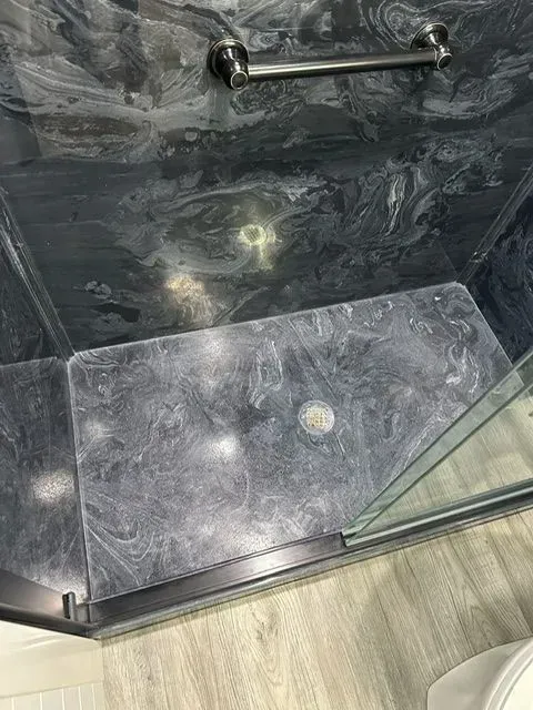 Shower with dark, marbled tile and glass door, showing water stains and a towel bar.