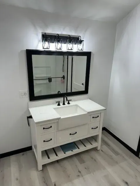 White bathroom vanity with black accents, rectangular mirror, and a five-light fixture.