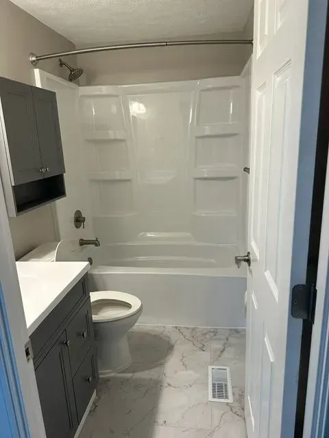 Bathroom with white tub/shower, gray vanity and cabinet, marble-look floor, and open white door.