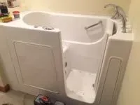 White walk-in bathtub with open door in a bathroom. Faucet on the side. Tools visible.