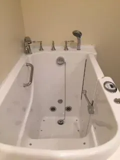 White walk-in bathtub with showerhead and faucet fixtures against a light-colored wall.