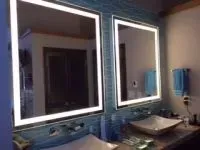 Two illuminated square mirrors above bathroom sinks. Blue tile background.