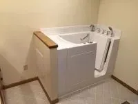 White walk-in bathtub in a bathroom with a tiled floor and beige walls.