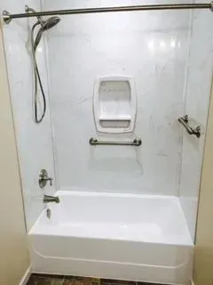 White bathtub and shower combo with grab bars, soap dish, and showerhead.