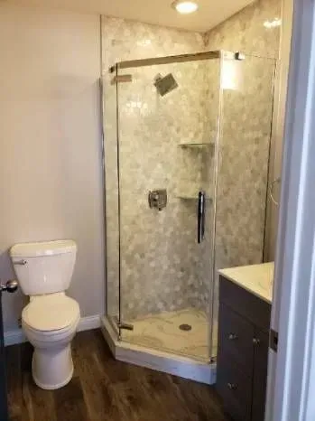 Bathroom with shower, toilet, and vanity. The shower has a glass door and patterned tile.