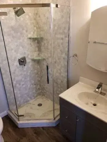 Bathroom with a glass shower, vanity, and light-colored hexagon tile.