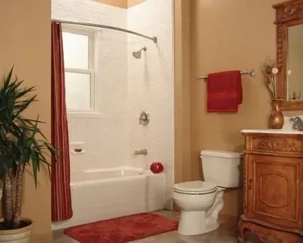 Bathroom with a white tub and shower, red rug and towels, and a decorative wooden cabinet.