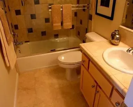 Bathroom with a tub, toilet, vanity, and tan tiles. Towels hang above the tub.