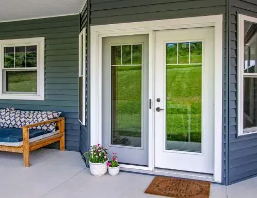 Exterior view of a house with a door, window, porch, bench, and plants; blue siding, white trim, and a doormat.