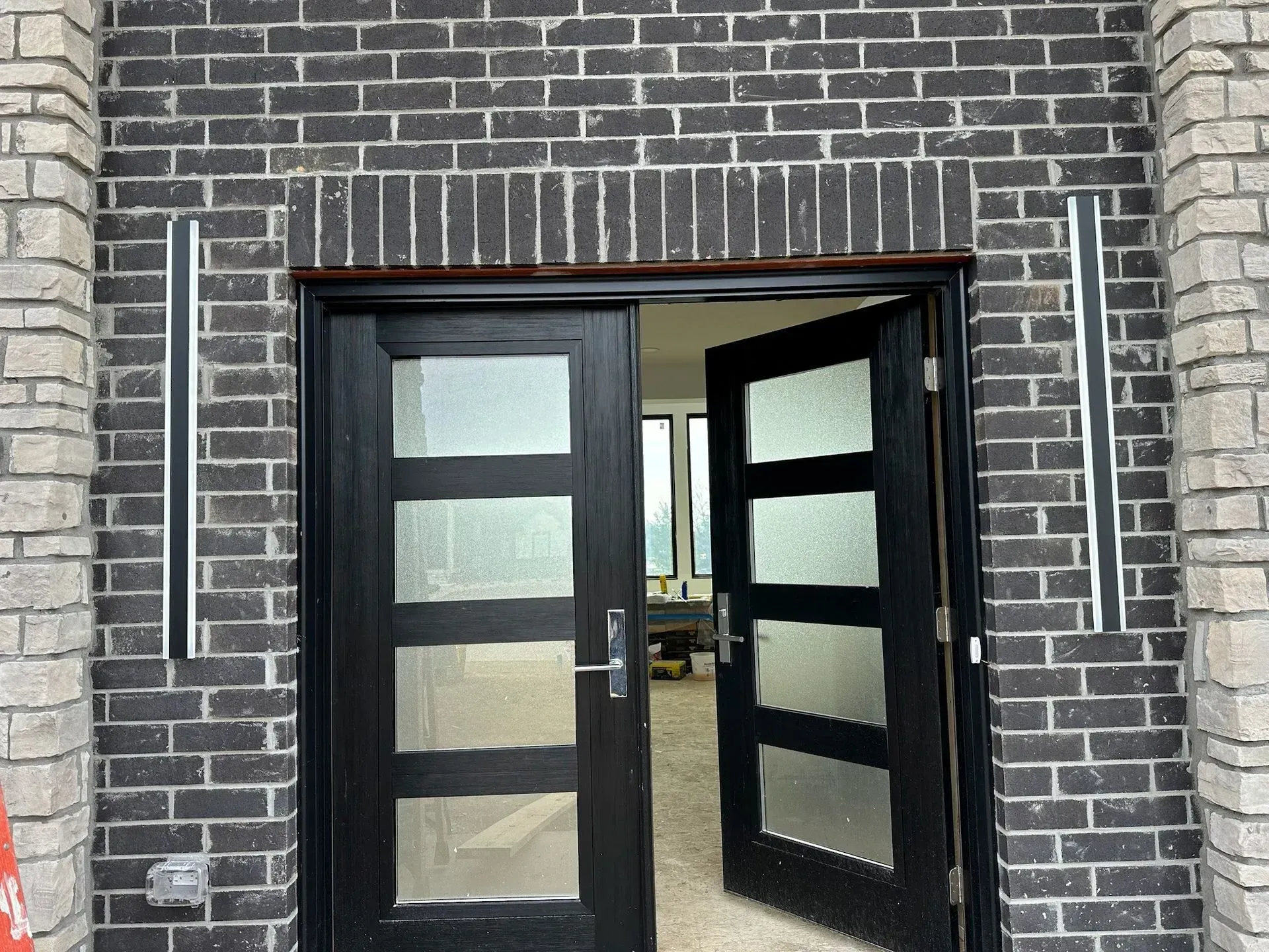 Black front doors with glass panels and sidelights in a brick facade.