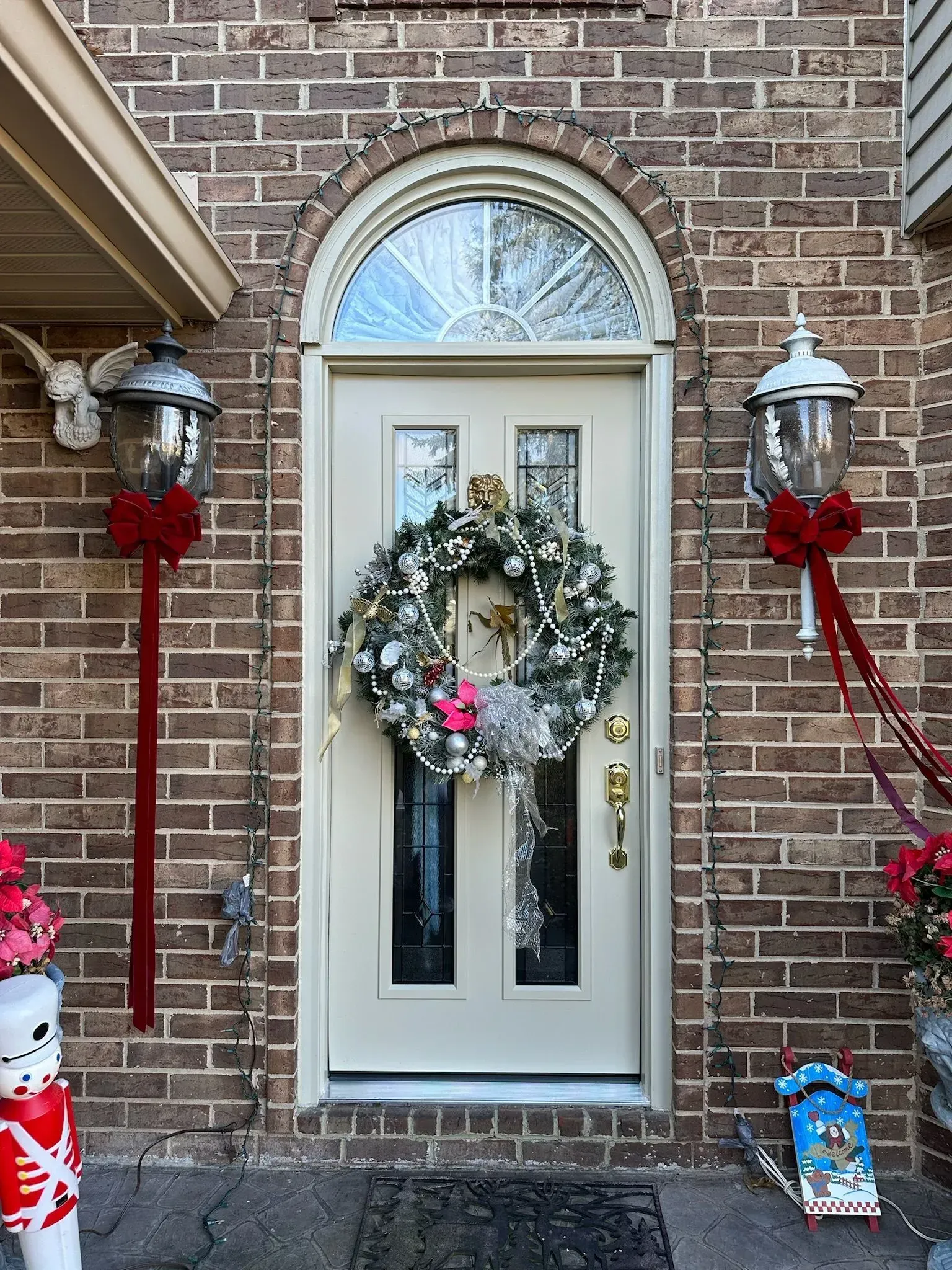Tan door with wreath, flanked by red-bowed lamps on brick building, Christmas decorations.