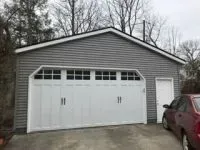 Gray garage with white trim and garage door; red car parked in front.