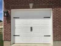 White garage door with decorative black hardware on a brick building.