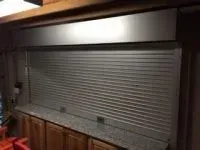 Closed metal roll-up shutter over a countertop and cabinets.