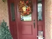 Red door with fall wreath, flanked by sidelights, brick exterior.