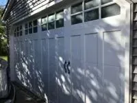 White garage door with windowed top panels, black handles, and gray siding.