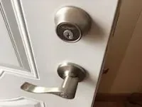 Silver door lockset on a white door. Top is a round deadbolt, bottom is a lever handle.
