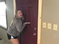 Woman gesturing enthusiastically toward a maroon door in a room under construction.