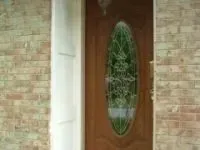 Wooden door with oval-shaped stained glass window, flanked by brick walls and a white door frame.