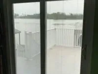 Sliding glass door looking out onto a flooded deck and river, overcast sky. White railings.