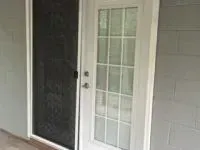 White-framed glass door next to a black screen door on a gray building.