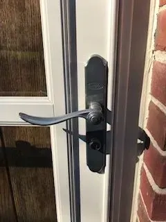 Black door handle on a white door frame, beside a brick wall.