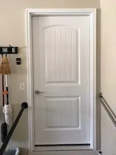 White door with vertical paneling, leading from a room to a garage.  Handle on left side.
