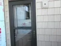 Dark gray door with screen, white siding, security camera.