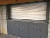 Gray outdoor bar with shutters and countertop against a cinder block wall.