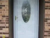 White front door with oval glass panel, gold handle, set in a brown brick wall.