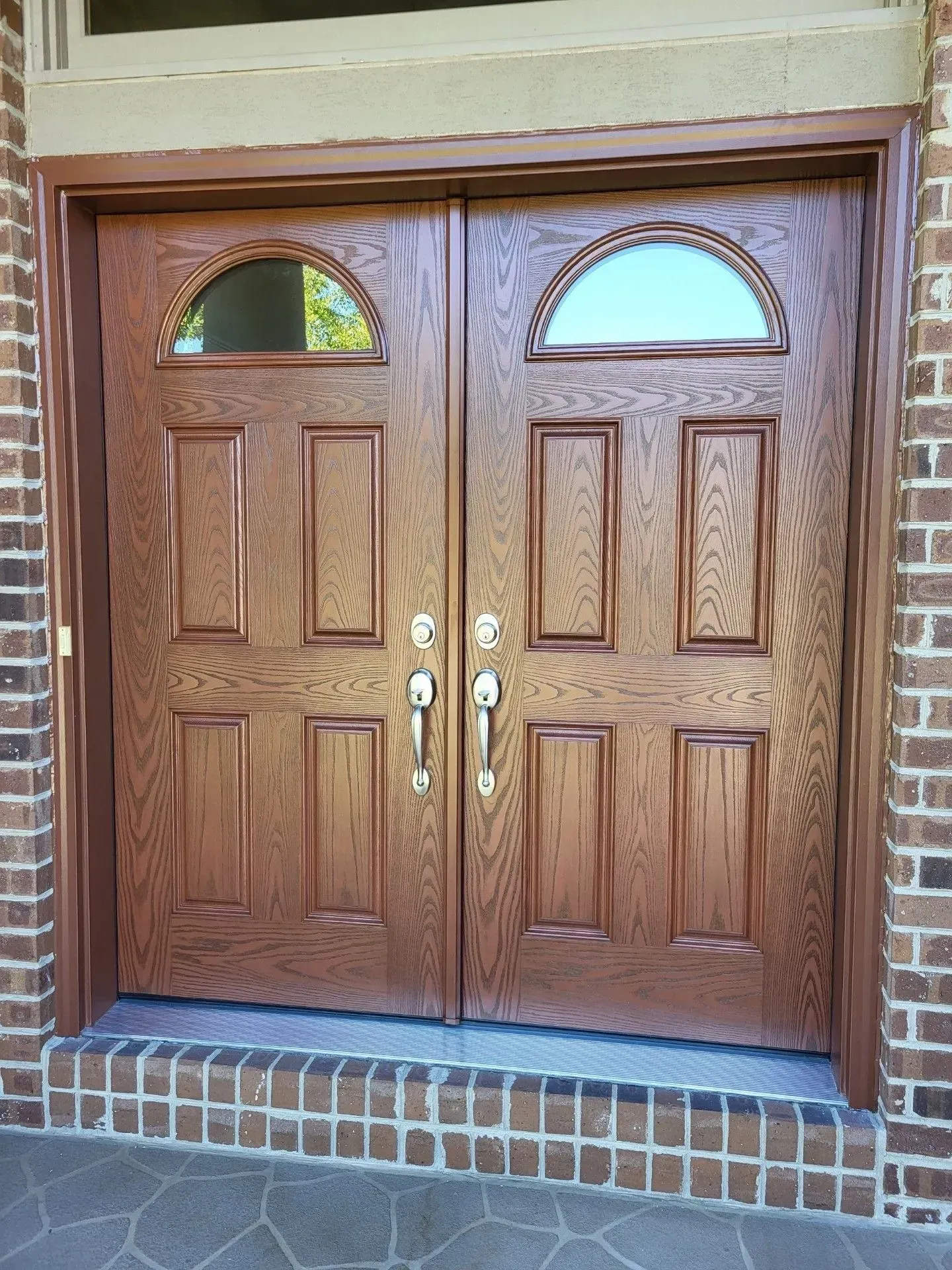 Double wooden front doors with arched glass windows, brick and stone exterior.