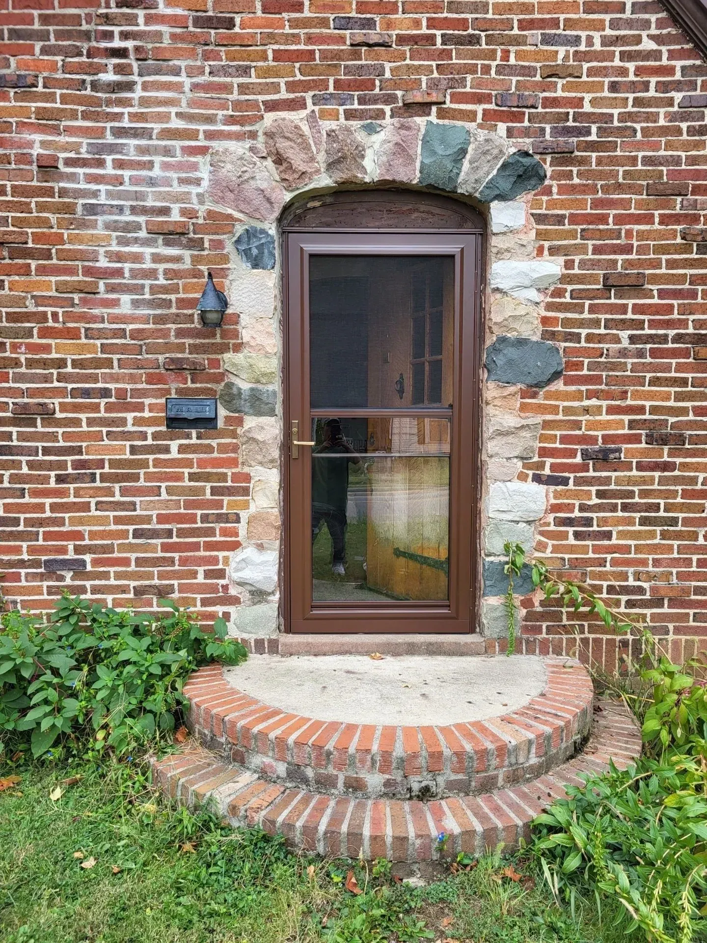 Brick building entrance with brown door and stone archway above. Brick steps at the door.
