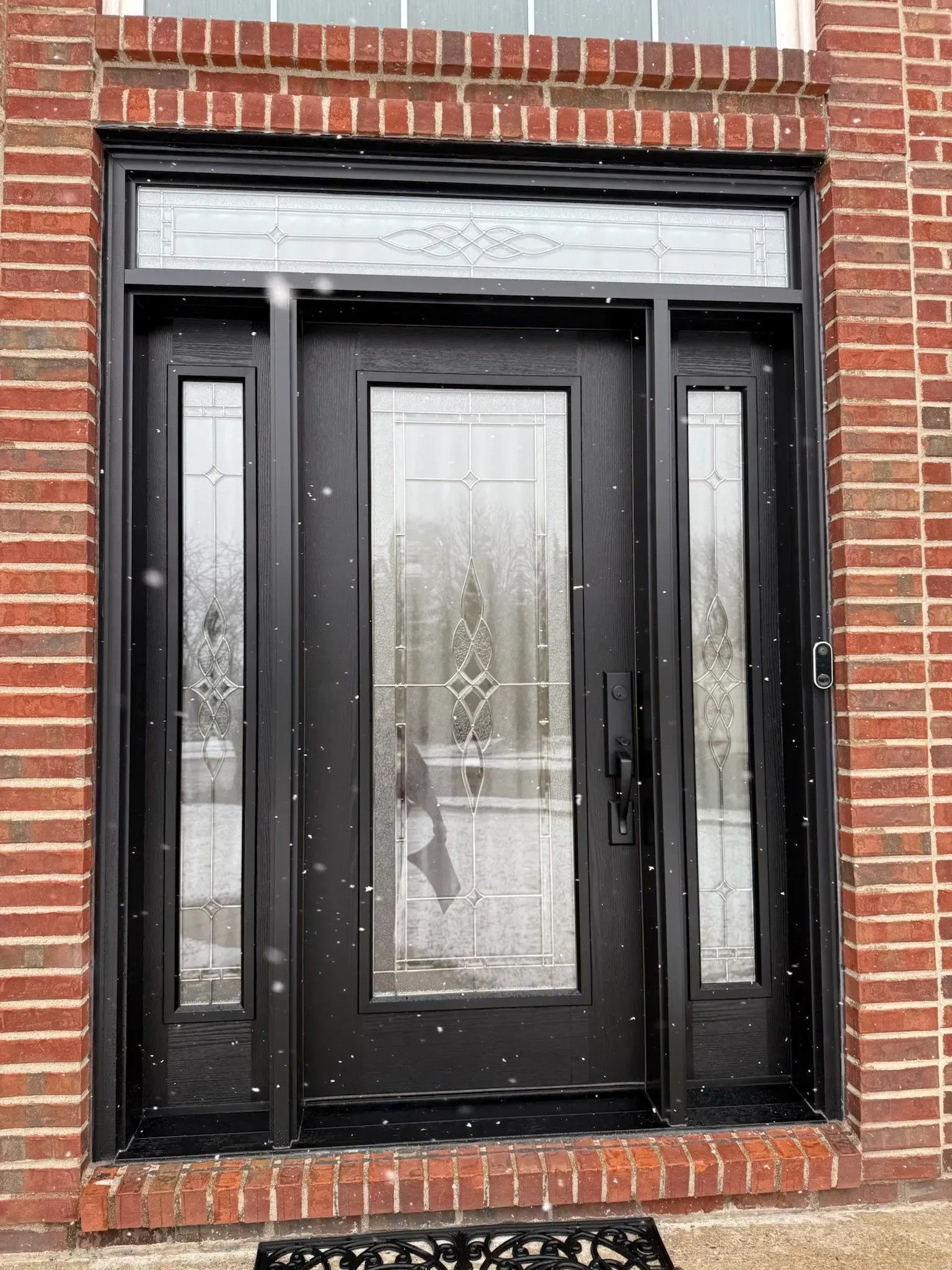 Black front door with sidelights and transom, set in red brick wall.