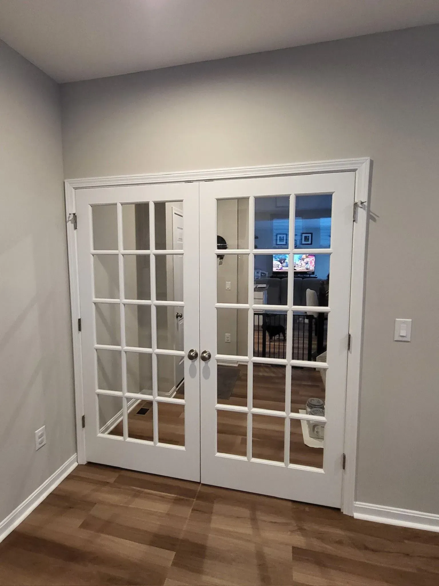 White French doors with multiple glass panes in a room with light gray walls and wood flooring.