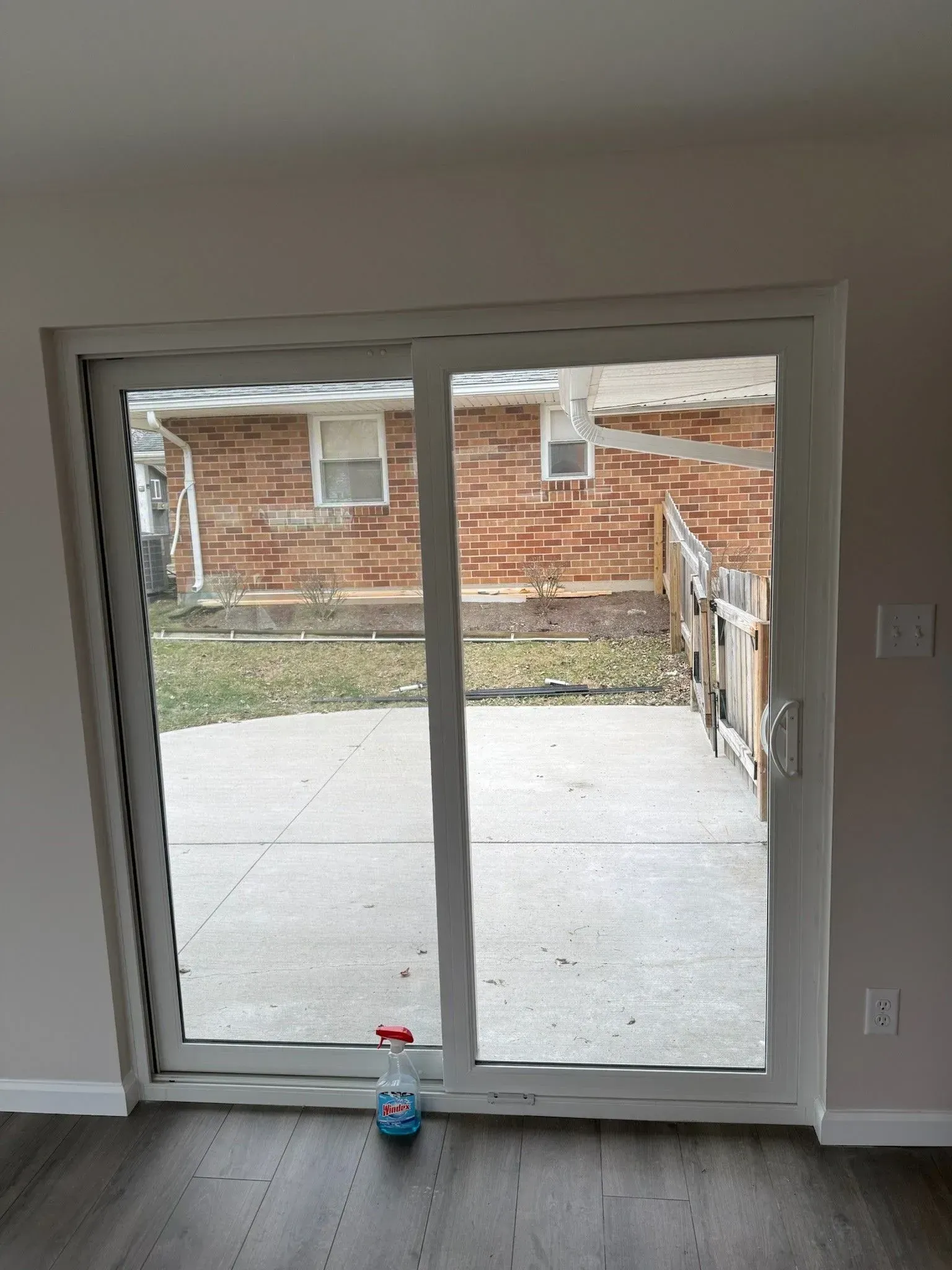 Sliding glass door looking out onto a patio and brick building in the backyard, a water bottle rests on the floor.