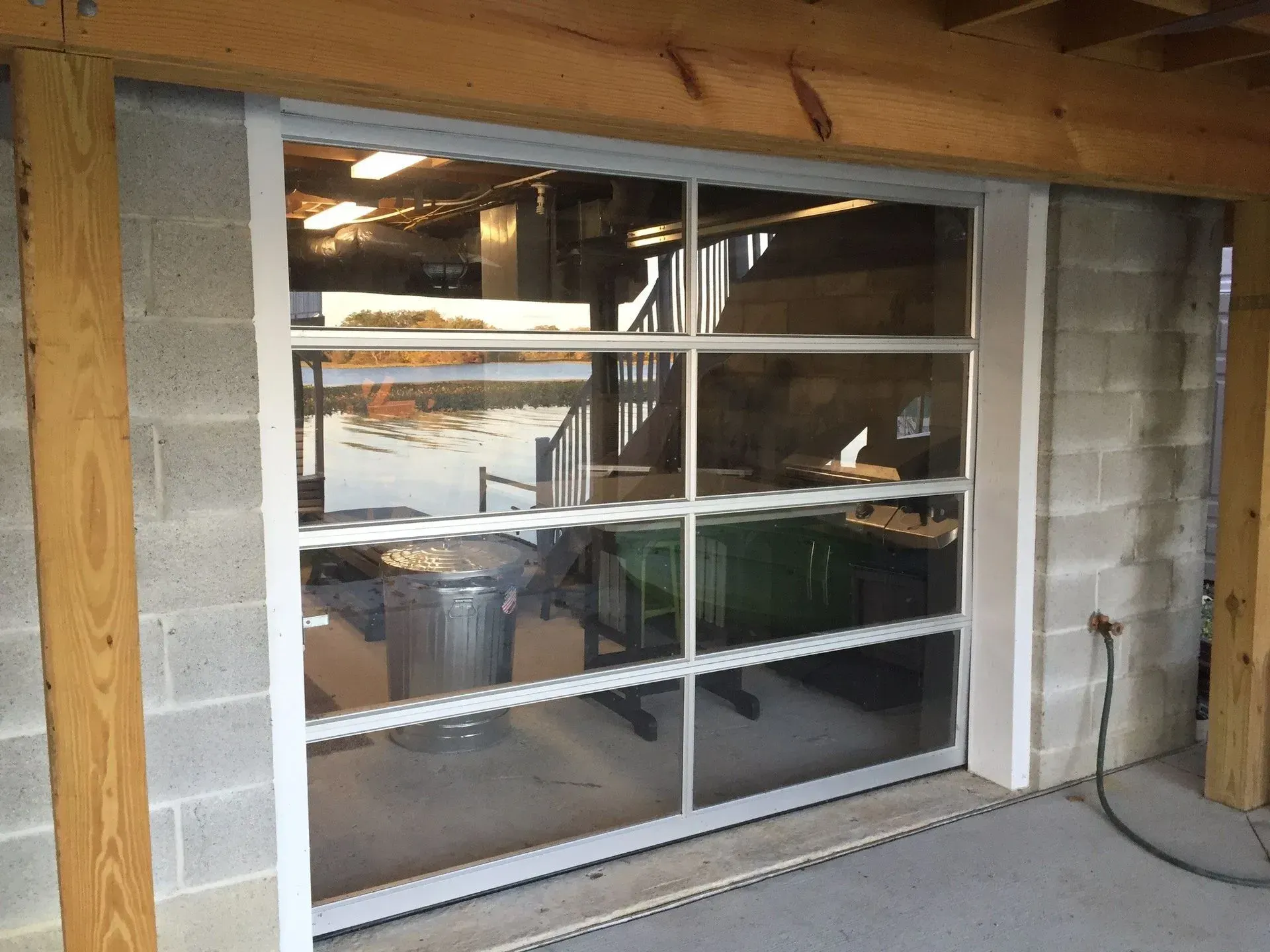 White-framed window in a cinderblock wall, reflecting a cluttered interior. Wood beams above and to the sides.