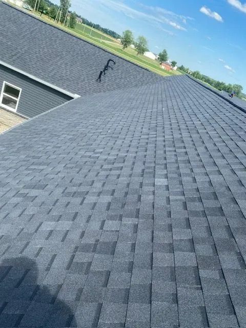 Dark gray asphalt shingle roof on a house, bright sunny sky.
