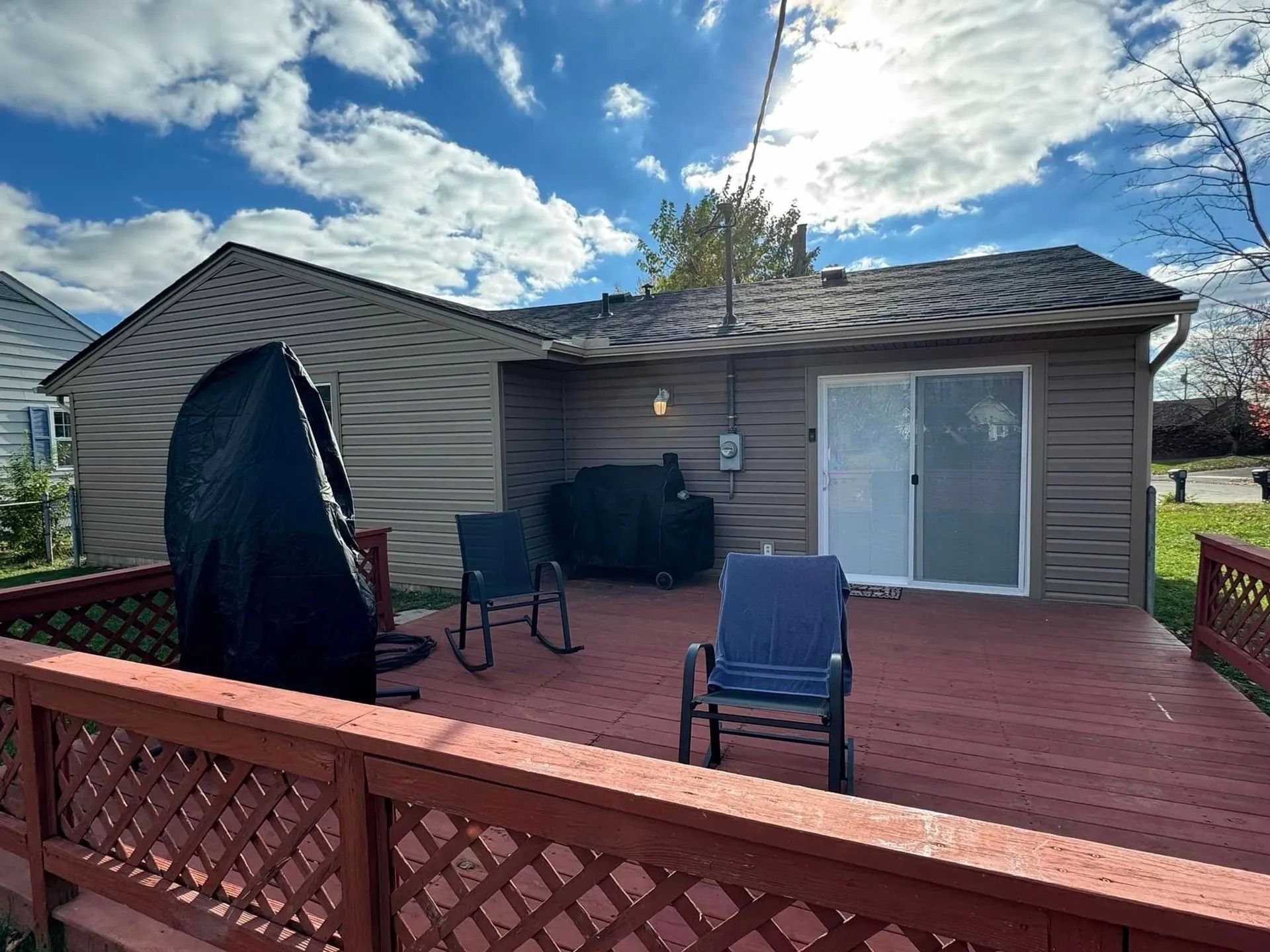 Backyard deck with red railing, two chairs, grill, and covered swing under a cloudy sky.