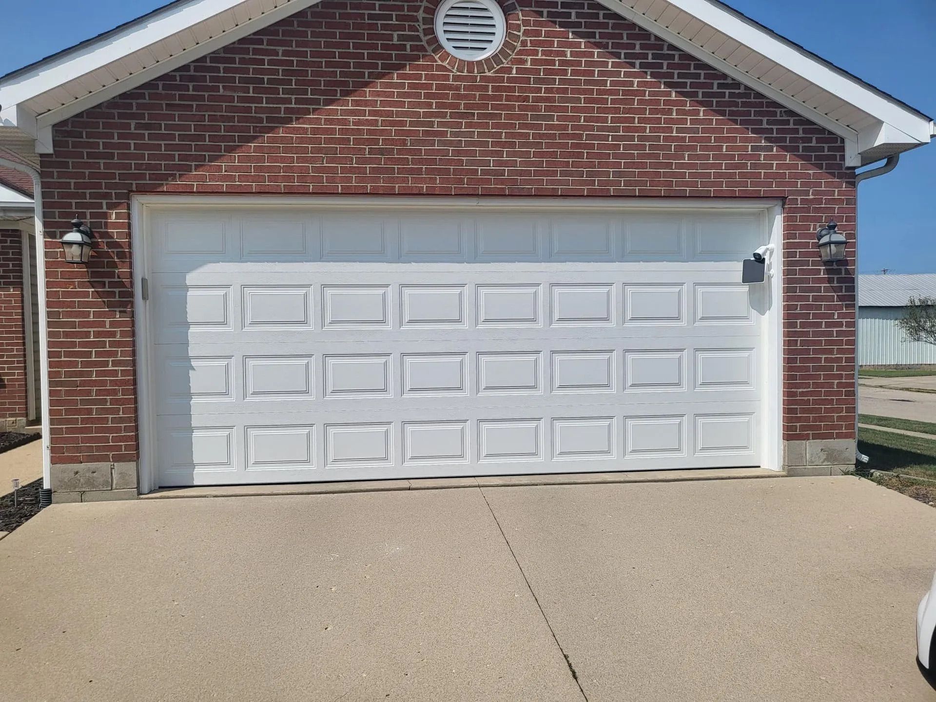 White garage door on a brick building with concrete driveway; lights on either side.